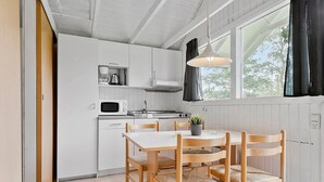 A compact kitchen with white cabinets, a microwave, a sink, and a dining table with four chairs. - First Camp Ajstrup Strand (Malling)
