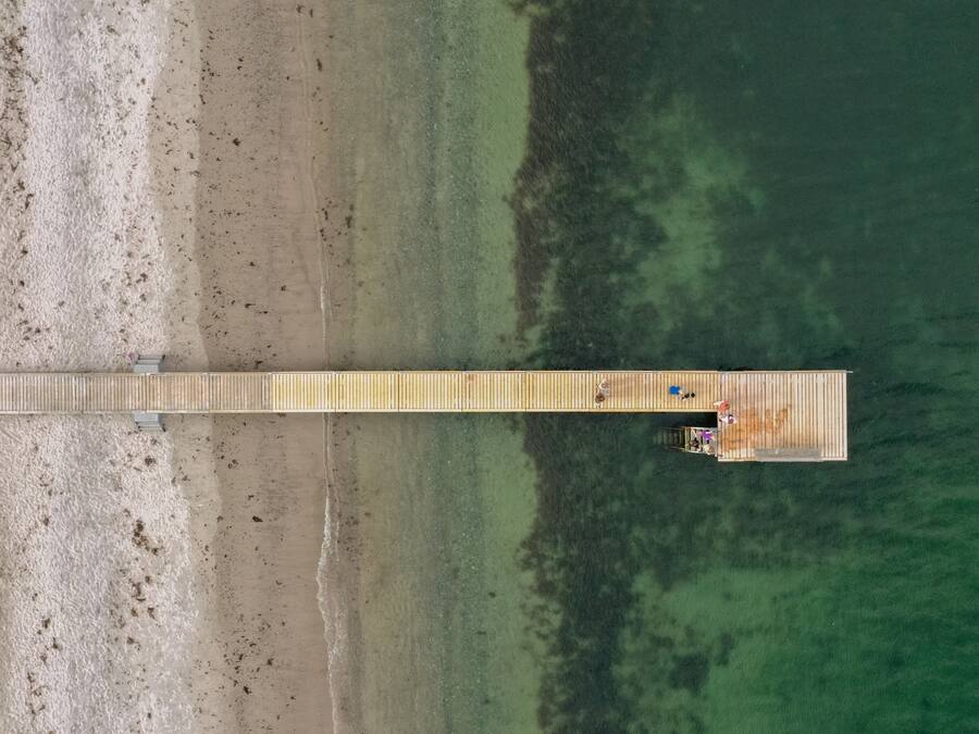 Vista aérea de un muelle de madera que se adentra en una masa de agua, con una pequeña construcción al final.