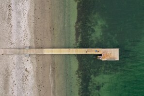 An aerial view of a wooden pier extending into a body of water, with a small structure at the end.