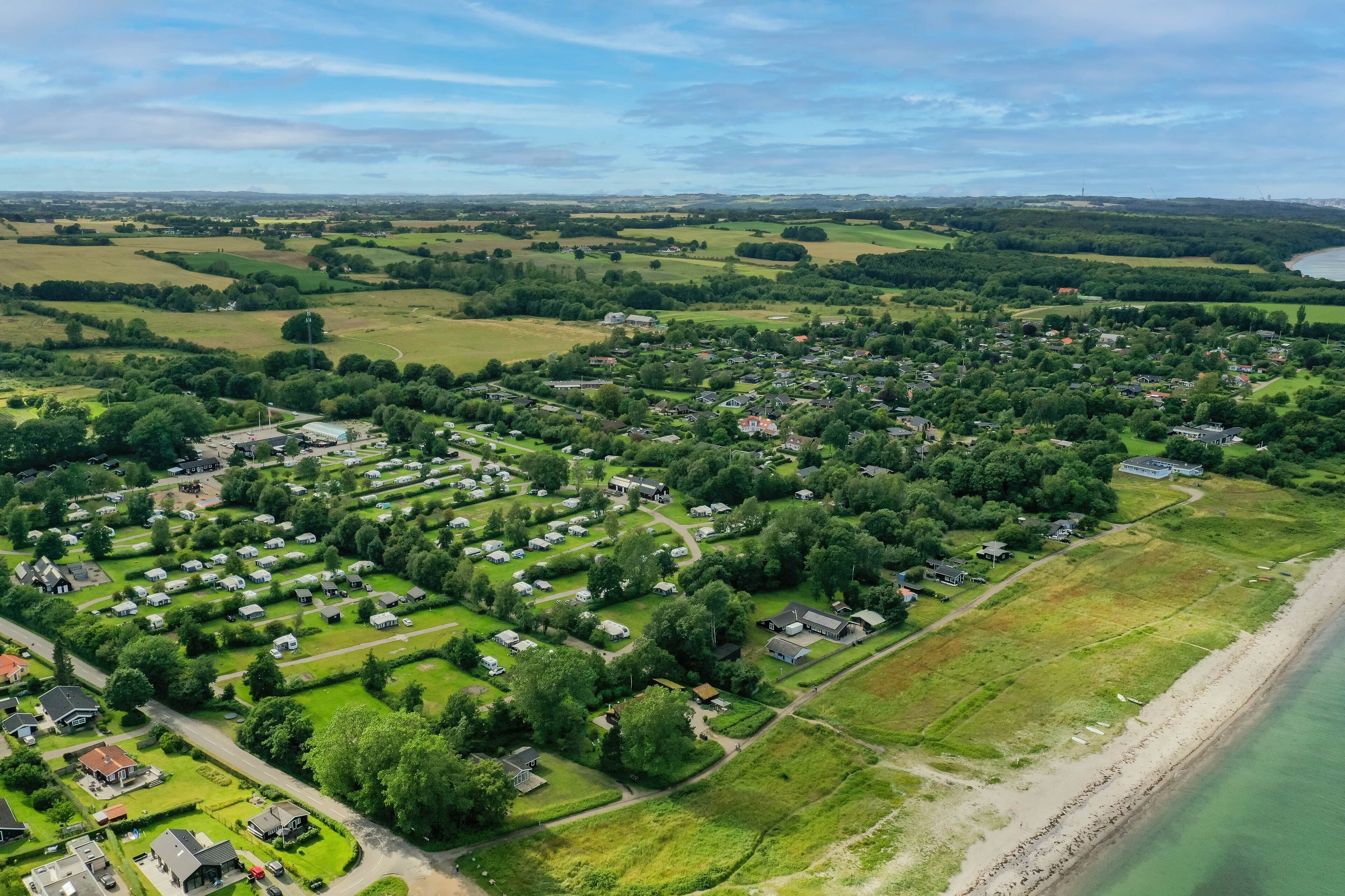 An aerial view of a coastal residential area with houses, green fields, and a beach.