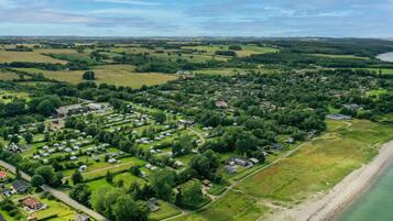 An aerial view of a coastal residential area with houses, green fields, and a beach.