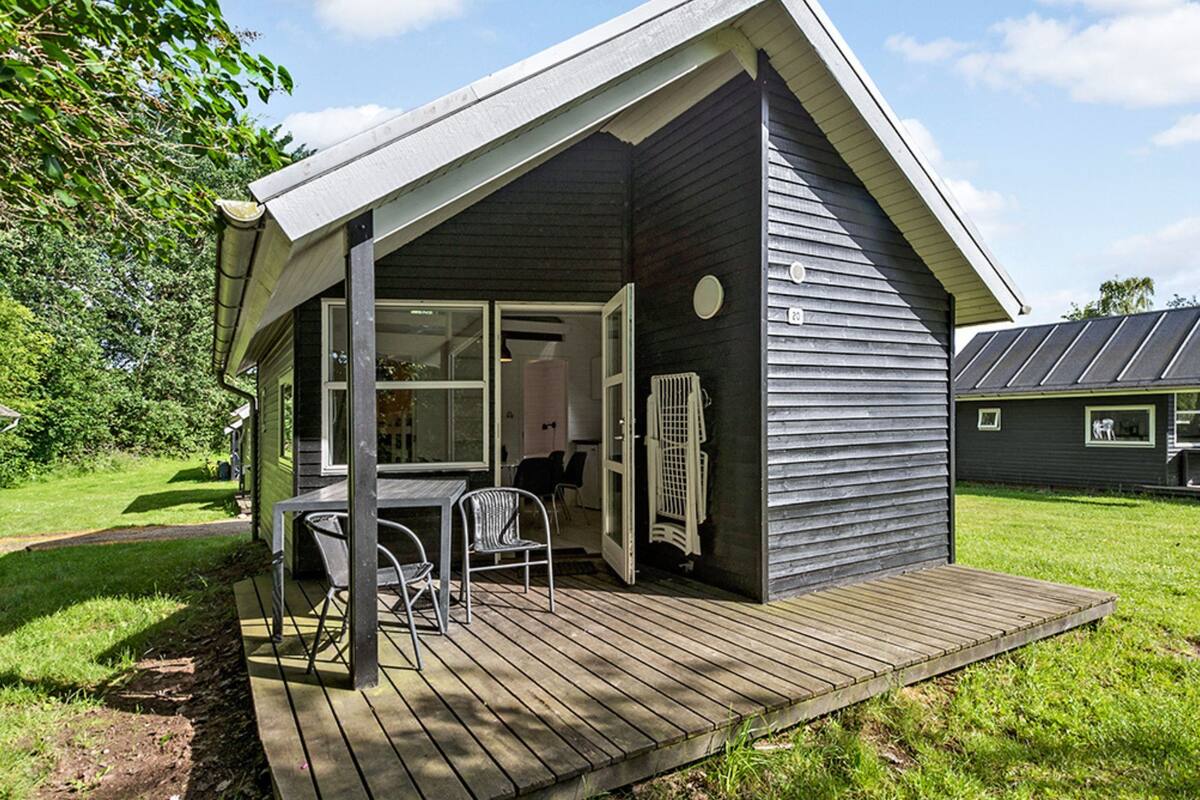 A small, dark-colored house with a wooden deck and a covered porch.