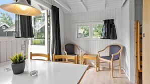 A room with a white ceiling, wooden walls, a white table, two wooden chairs, a potted plant, and a window with curtains.