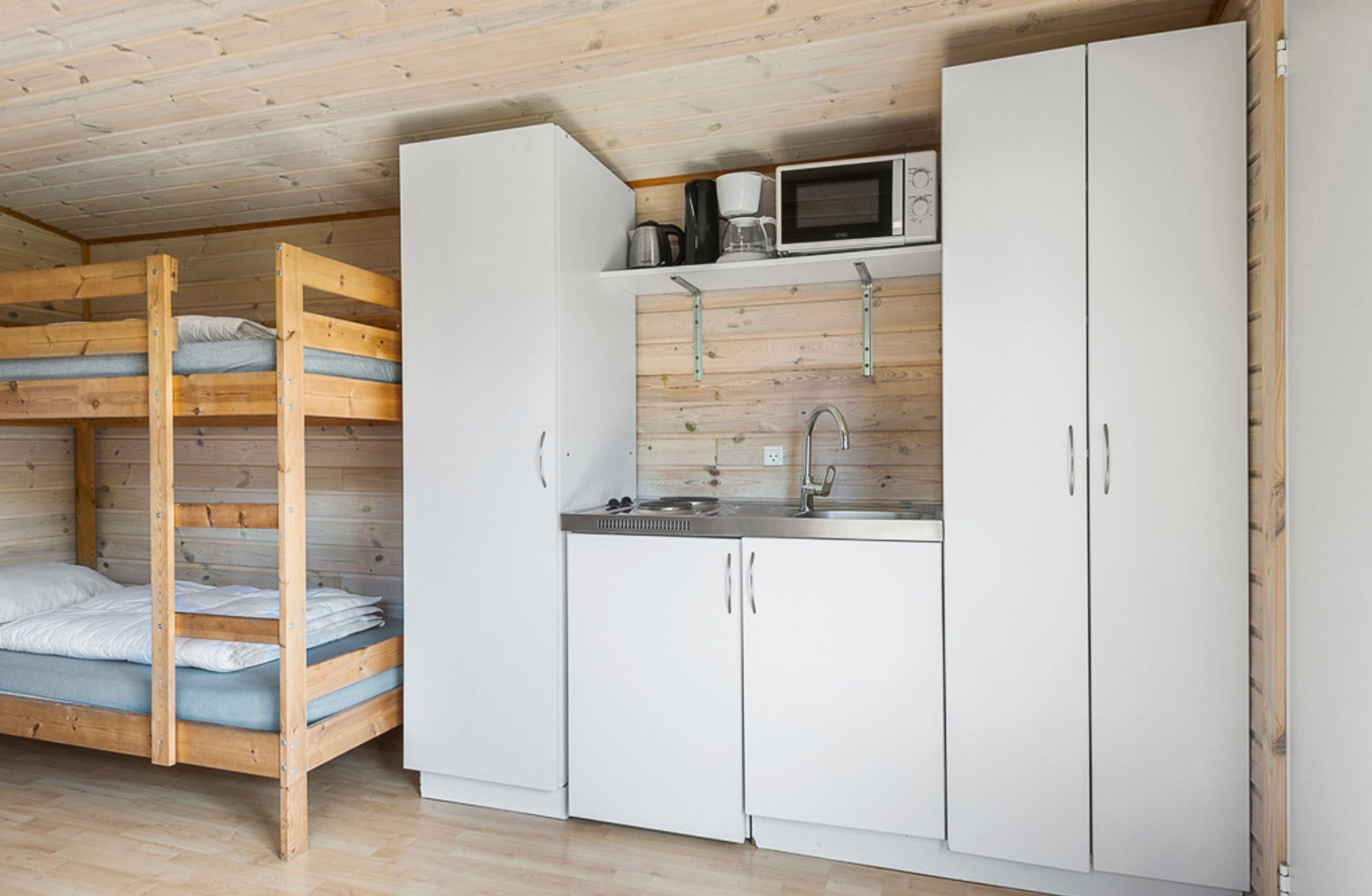 Una cama litera con escalera de madera, una kitchenette con microondas y armarios blancos.