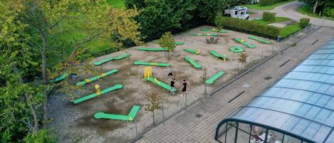 An outdoor area with green exercise equipment, a covered walkway, and a fenced play area.