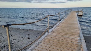 A wooden pier extending into calm waters with a metal railing, leading to a small structure on the right. - First Camp Ajstrup Strand (Malling)