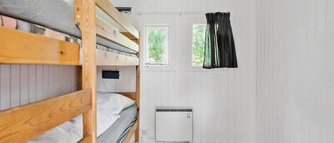 A small, clean room with bunk beds, a window, and a radiator.