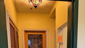 Un pasillo con piso de baldosas, una puerta de madera con un vitral y una lámpara en el techo.