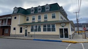 Un edificio de dos pisos con techo verde, un letrero que indica bar y parrilla, y un cartel de 'No Entrar' en la acera.