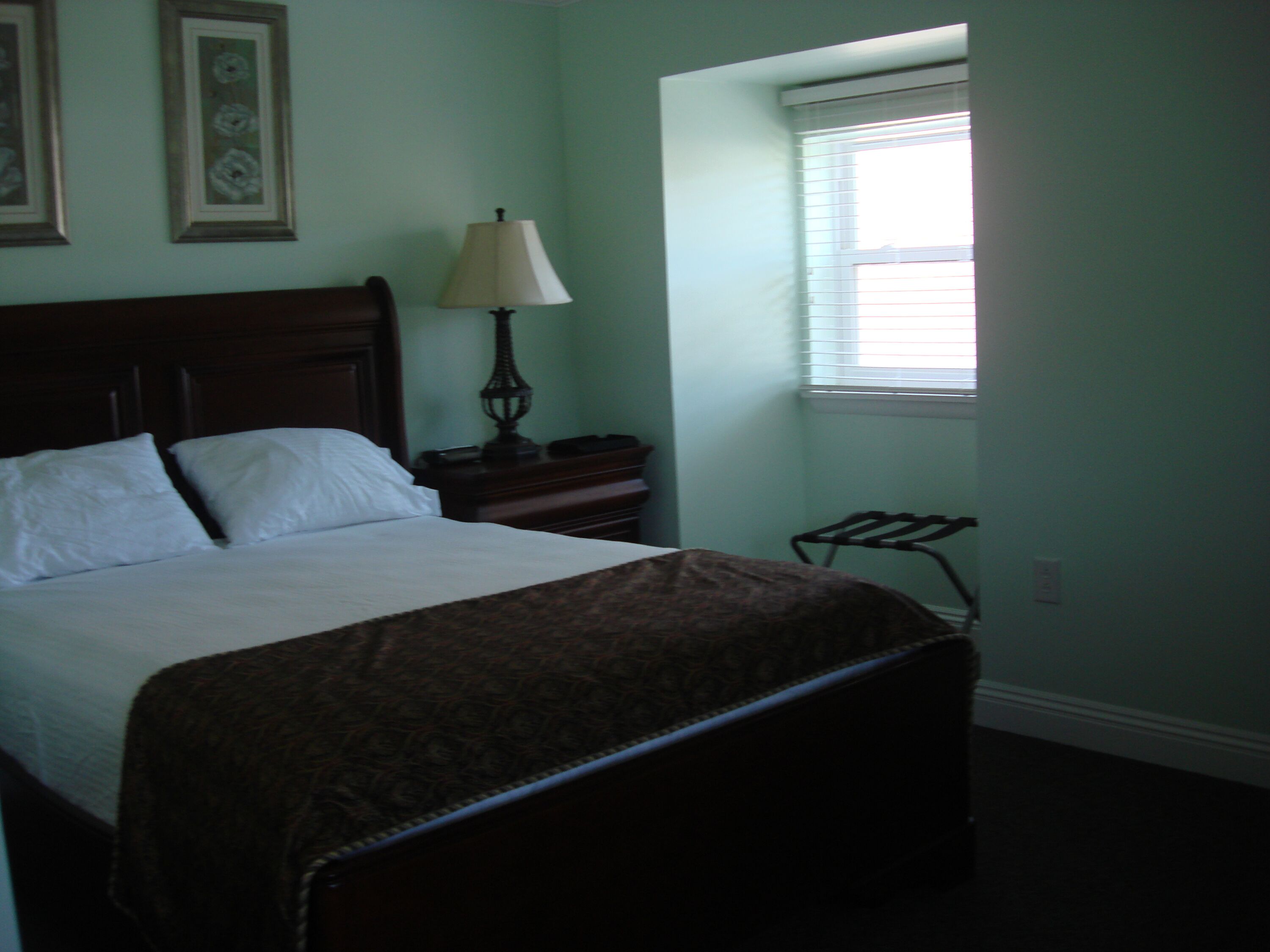 A bedroom with a bed, a nightstand, a lamp, and a window.