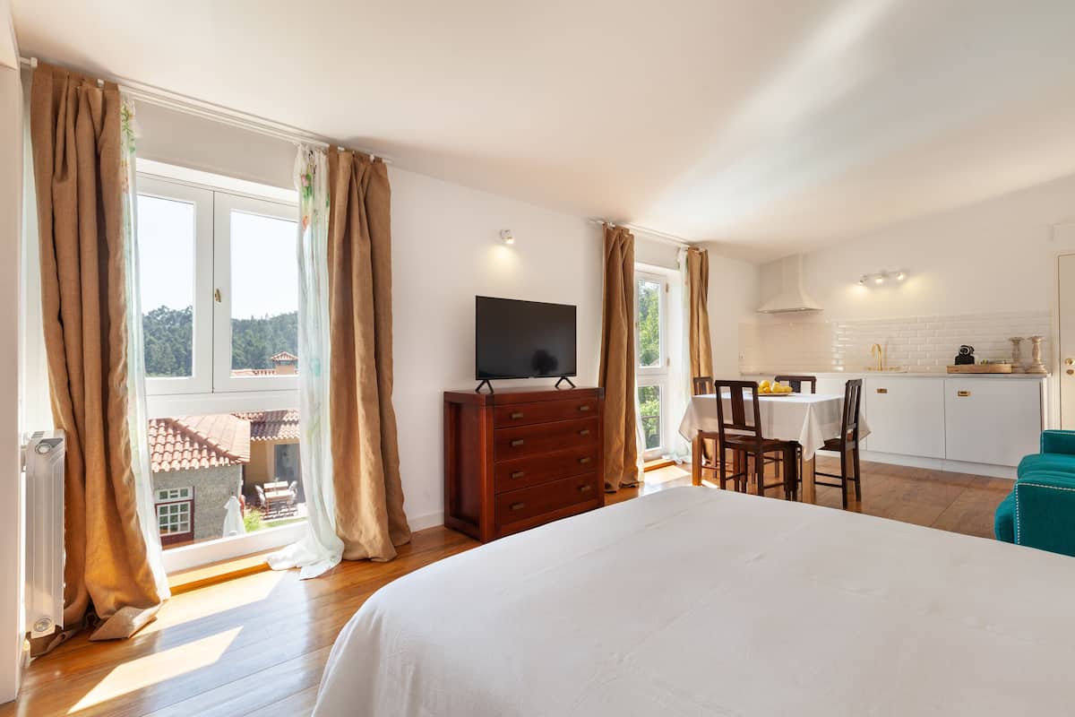 Une chambre dotée d’un grand lit, d’une commode, d’une télévision et donnant sur un balcon avec un coin repas.