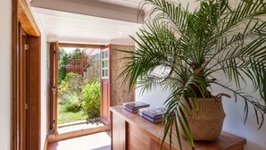 Un bureau en bois orné d’une plante en pot et de quelques livres, une porte-fenêtre donnant sur un jardin, et un plafond doté d’un éclairage encastré.