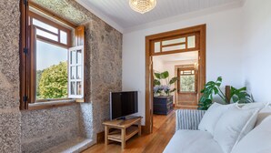 Une pièce avec un plancher en bois, un canapé blanc, un téléviseur posé sur un meuble et un mur en pierre.