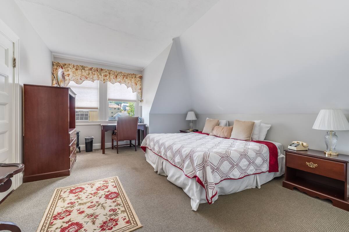 Un dormitorio con una cama grande, un escritorio, una silla, un armario y una ventana con cortinas.