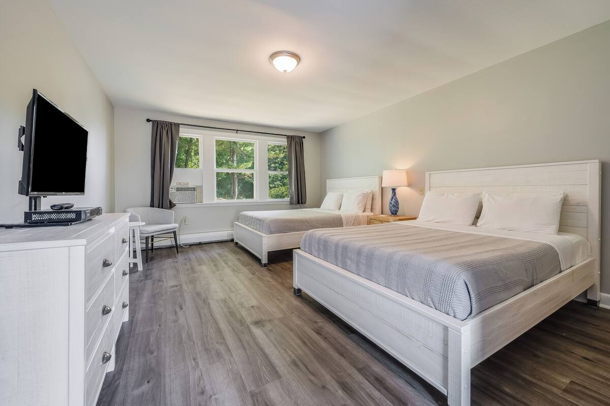 Una habitación de hotel con dos camas, un escritorio, un televisor y una ventana con cortinas.