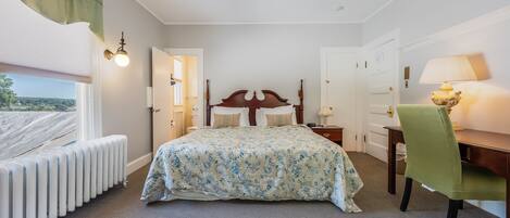A bedroom with a bed, a desk, a chair, a radiator, and a lamp.