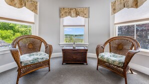 A corner room with two wicker chairs, a small wooden chest, and a window with a view of greenery. - Castle Manor Inn (Gloucester)