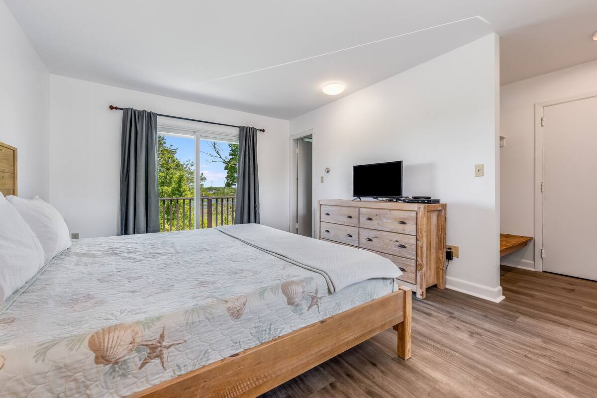 Un dormitorio con cama, cómoda, televisor y balcón.