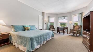 A bedroom with a bed, a desk, two chairs, a dresser, and a TV.