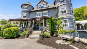 A large, two-story house with a wrap-around porch and a stone foundation. - Castle Manor Inn (Gloucester)