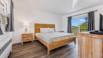 A bedroom with a wooden bed, a bedside table with a lamp, a TV on a wooden stand, and a window with curtains.