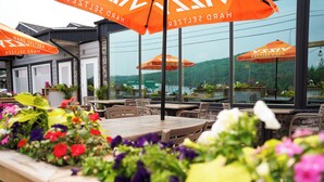 An outdoor seating area with tables and chairs, surrounded by potted plants and orange umbrellas.