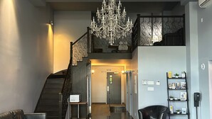 A spacious lobby with a chandelier, a staircase, a reception desk, and a seating area.