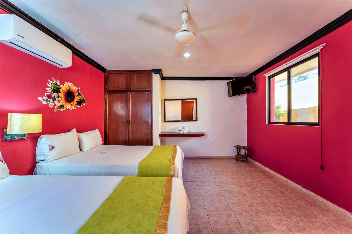 A hotel room with two beds, a ceiling fan, an air conditioner, a window, and a wall-mounted TV.