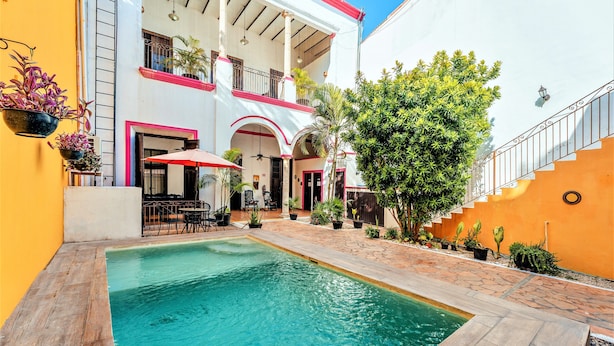 A courtyard with a swimming pool, outdoor seating, and a two-story building with balconies. - Hotel Gran Centenario (Mérida)