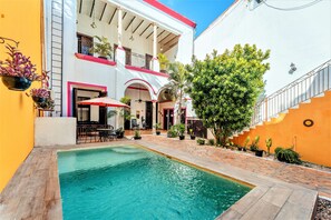 Un patio con piscina, mobiliario exterior y un edificio de dos plantas con balcones.