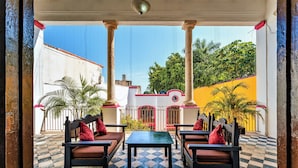 A covered patio with checkered flooring, a table, and four chairs with red cushions. - Hotel Gran Centenario (Mérida)