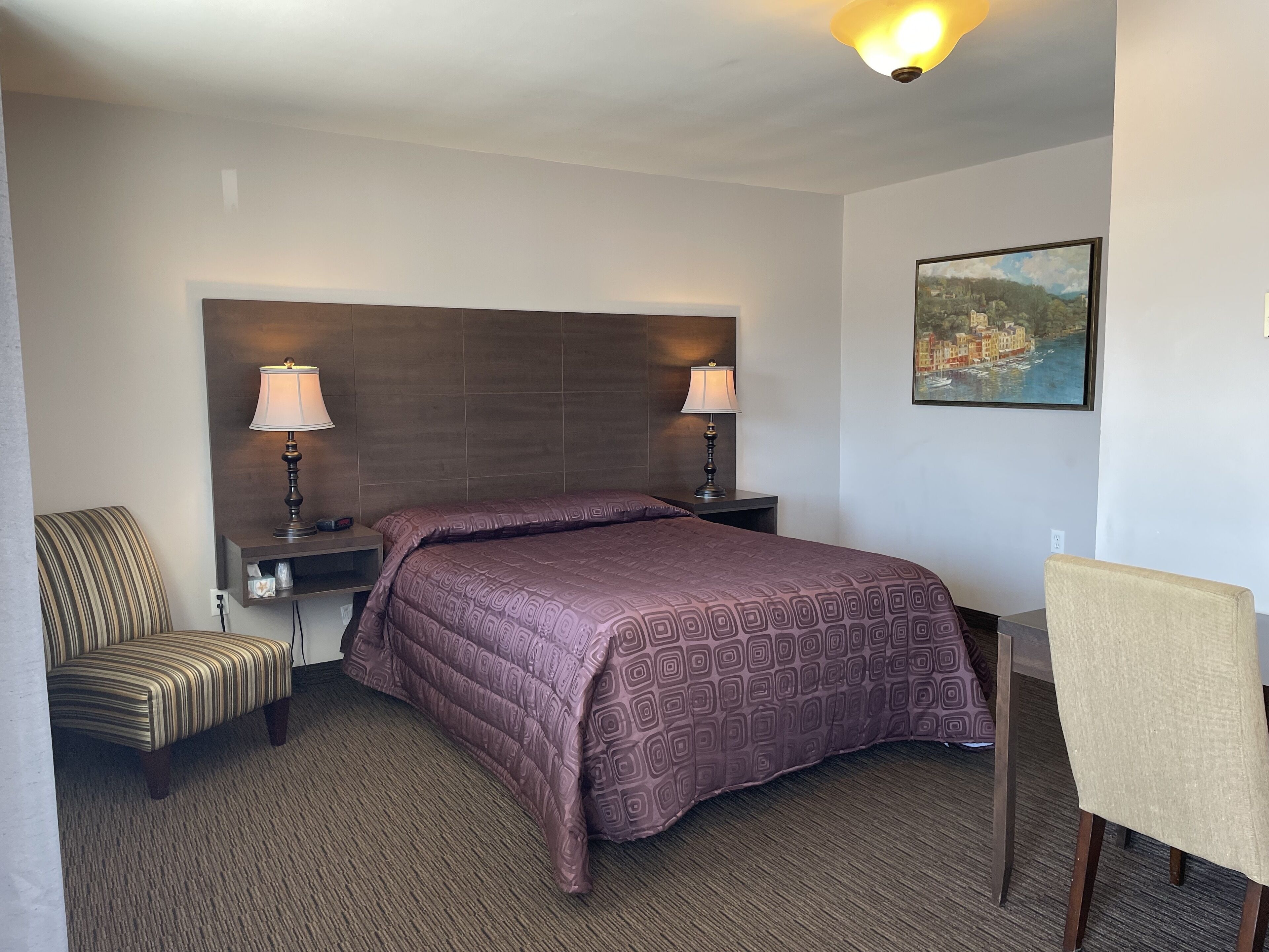 Habitació d'hotel amb un llit gran, dues làmpades de nit, una cadira, escriptori i un quadre a la paret.