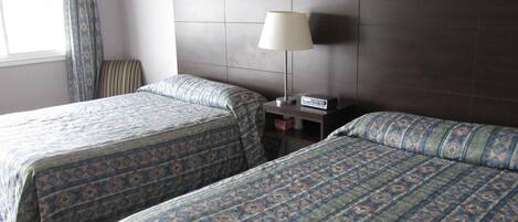 Habitación de hotel con dos camas, una mesita de noche, una lámpara y una ventana con cortinas.