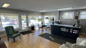 A reception area with a wooden floor, a reception desk, a green armchair, and a white armchair. - Winsome Inn (St. Stephen)