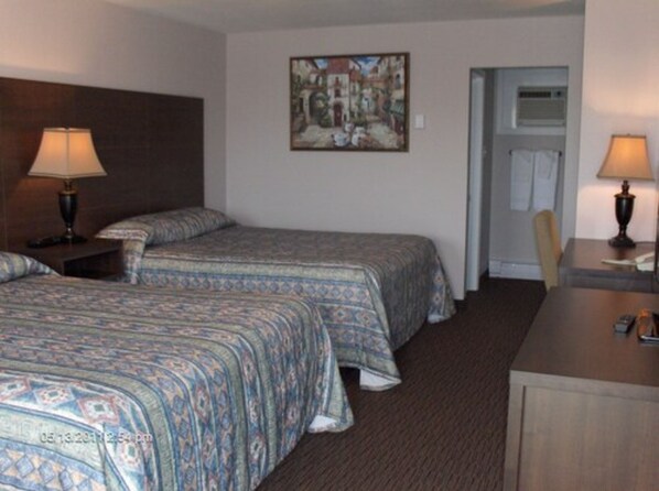 Habitación de hotel con dos camas, un escritorio, una silla, un cuadro en la pared y un equipo de aire acondicionado.