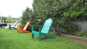 Un espacio verde con tres sillas Adirondack de diferentes colores.