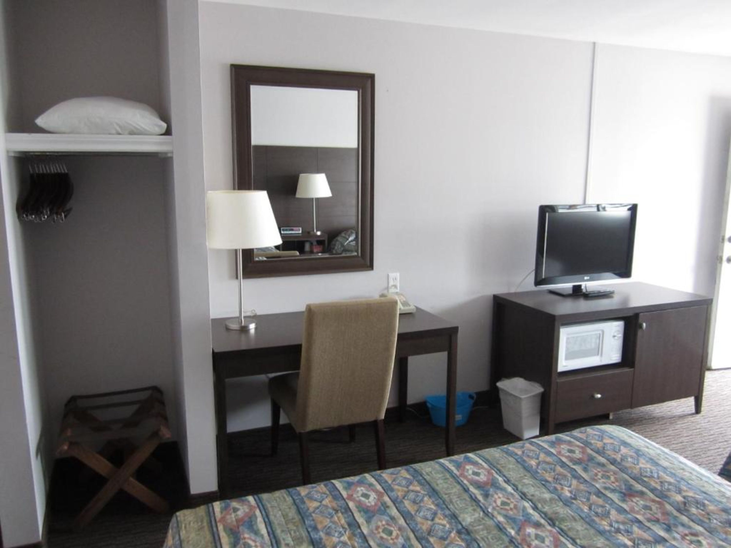 A hotel room with a bed, a desk with a chair, a television, a mirror, and a wardrobe.