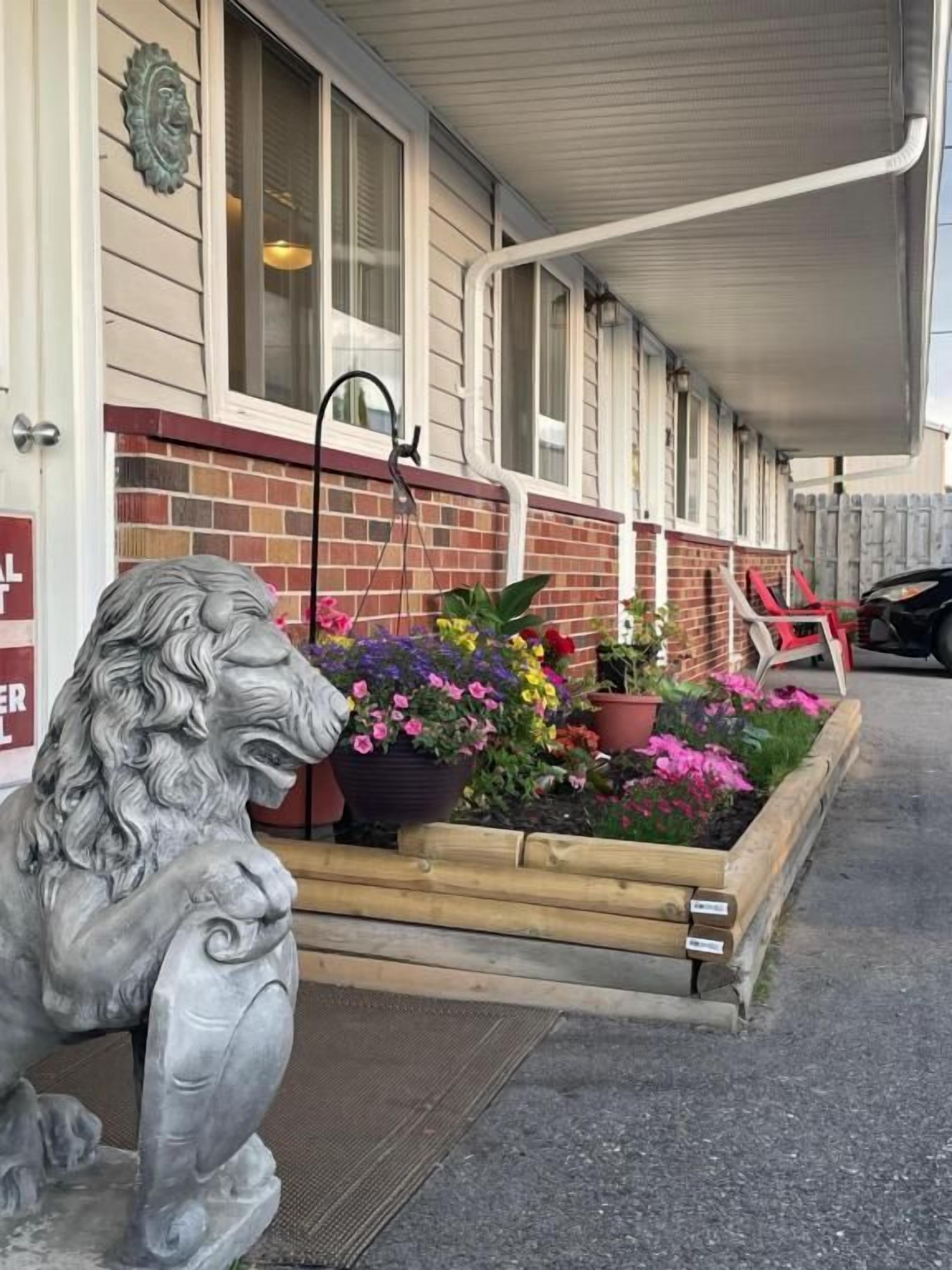 A building with a brick facade, a lion statue, and a flower bed with various plants.
