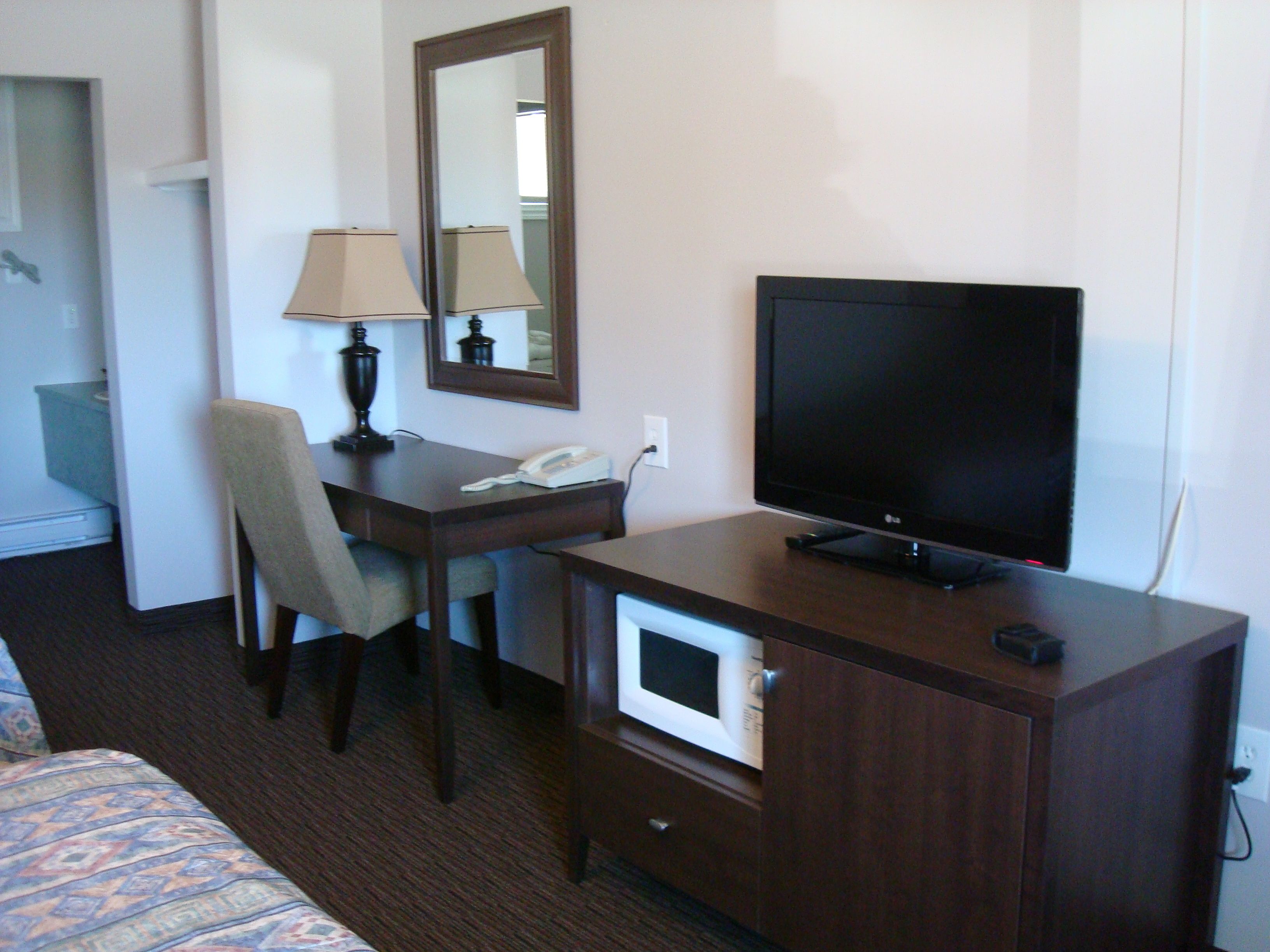 A hotel room with a bed, a desk with a lamp, a telephone, a television, and a microwave.