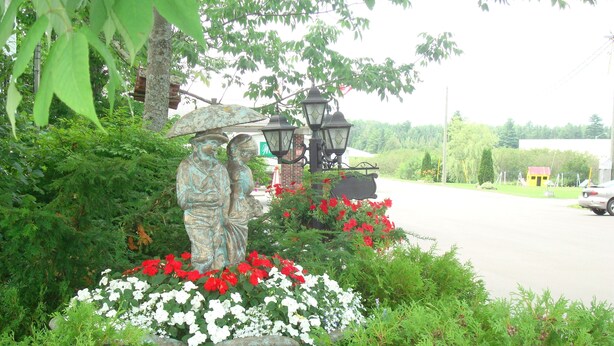 A garden with a statue, red and white flowers, and a street in the background. - Winsome Inn (St. Stephen)