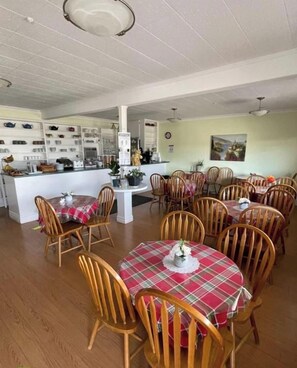 A dining area with multiple tables and chairs, a kitchen area with shelves, and a painting on the wall.