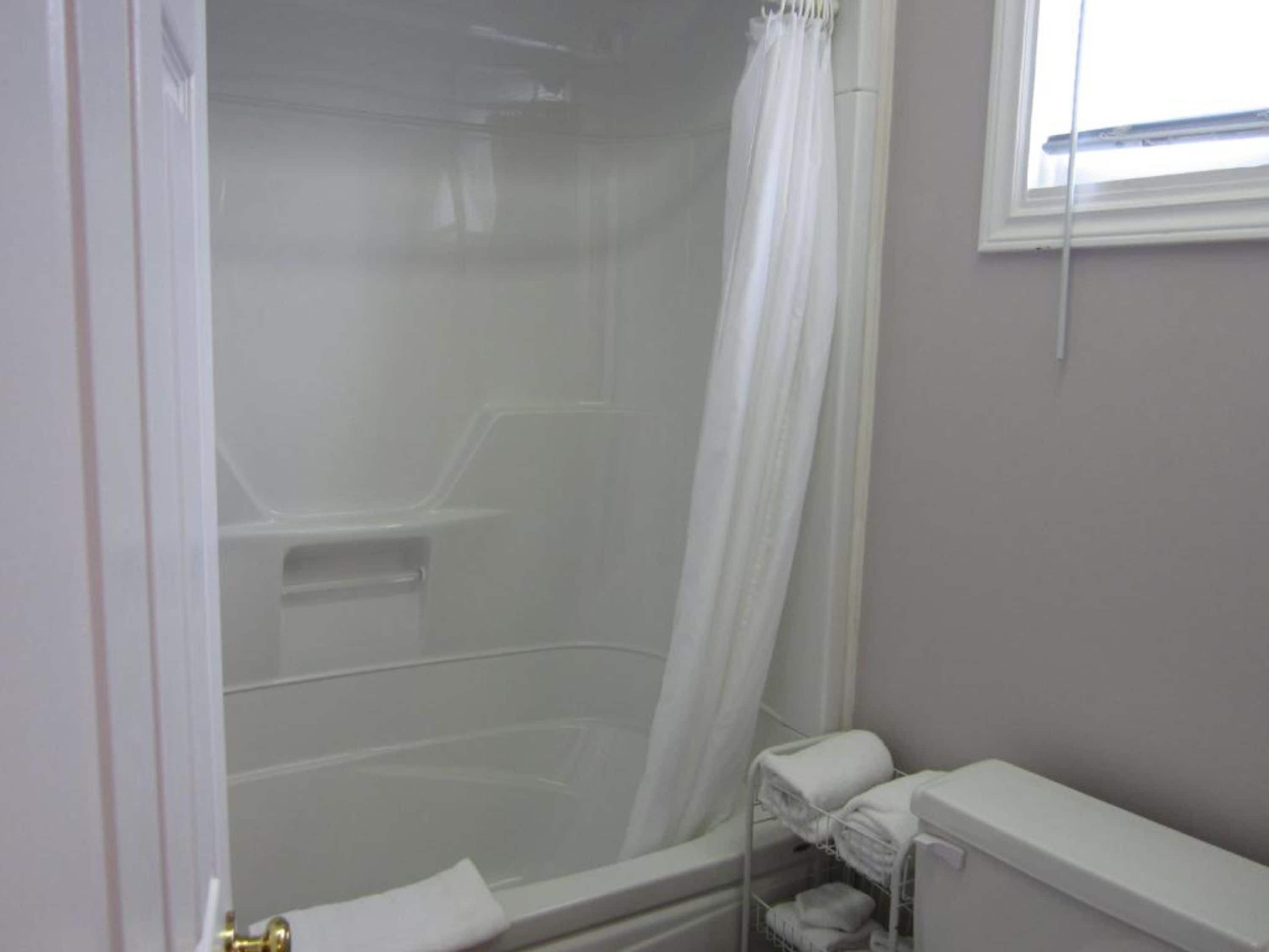 A bathroom with a shower, a toilet, and a window.