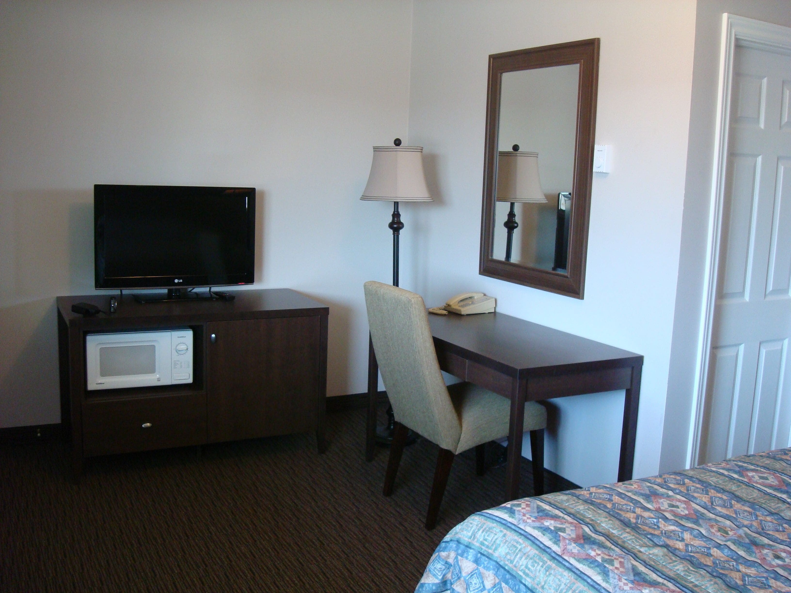 A hotel room with a flat-screen TV, a desk with a lamp, a telephone, and a microwave.