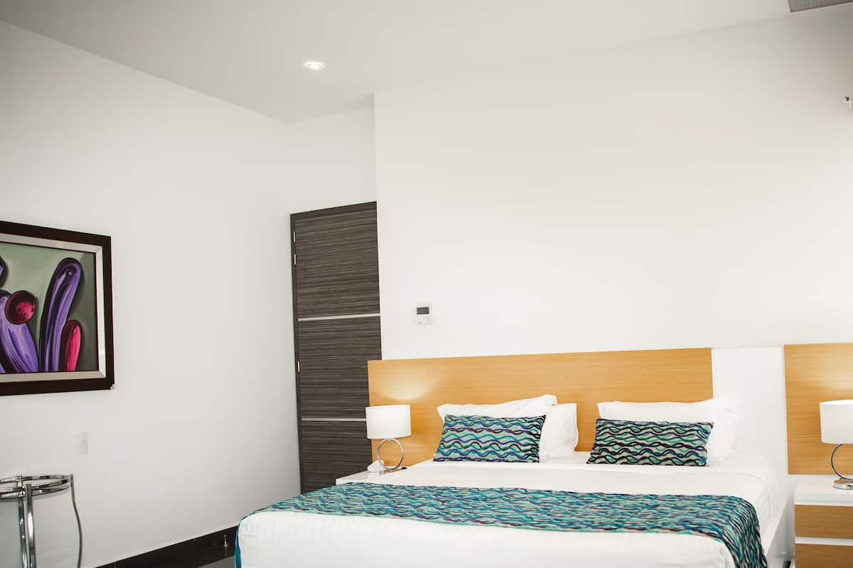 Una habitación de hotel con una cama, mesitas de noche, un calentador en la pared y un cuadro.