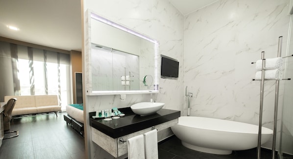 Une salle de bain moderne avec une grande baignoire, un meuble-lavabo avec un miroir et un canapé dans le salon attenant.