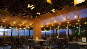 Un restaurant moderne offrant une vue panoramique, avec un plafond haut orné de motifs géométriques et un pilier central en bois.
