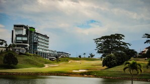 Un bâtiment moderne à plusieurs étages, doté d’une structure incurvée, entouré d’un terrain de golf et bordé par un plan d’eau.