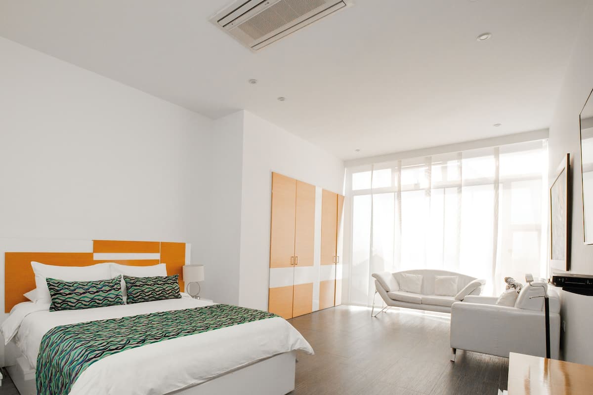 Una habitación de hotel con cama, mesita de noche, lámpara, armario y sofá.