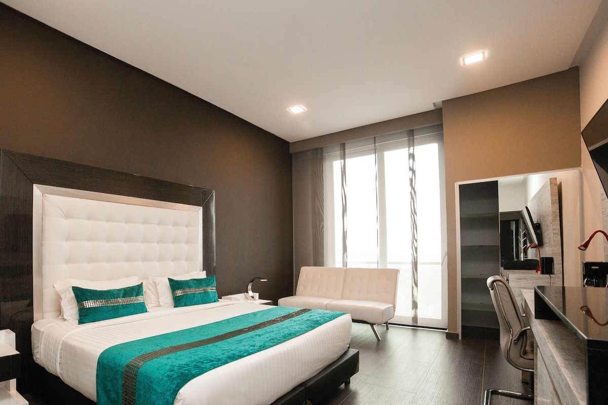 Una habitación de hotel moderna con una cama grande, una zona de estar y vistas al exterior.