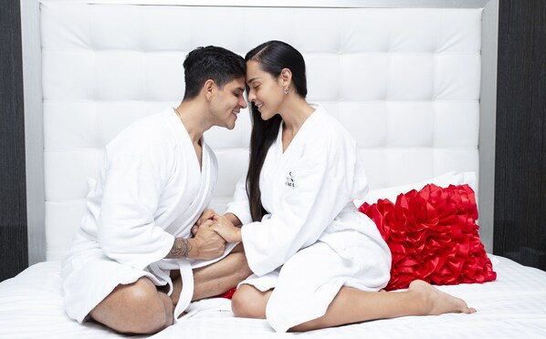 Un couple est assis sur un lit doté d’une tête de lit blanche et d’un coussin décoratif rouge.